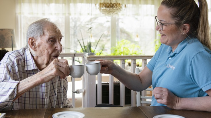 Äldre man och hemtjänstpersonal skålar med kaffekoppar