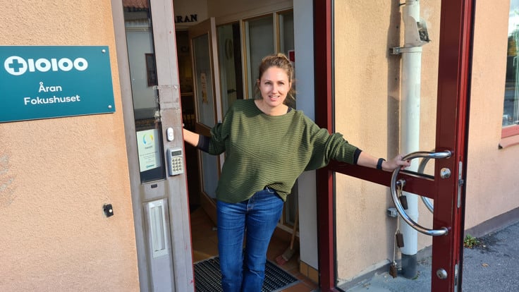 Kvinna håller upp dörr och ser glad ut. På en skylt intill dörren står Åran Fokushuset.
