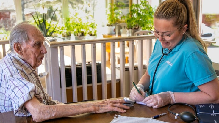 Kvinnlig personal antecknar värden från pulsmätare på äldre mans finger