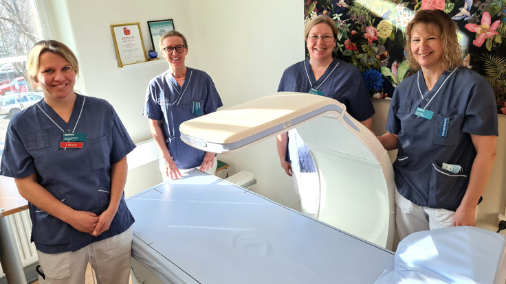 Fyra kvinnor i sjukvårdskläder samlade runt en röntgenapparat, en så kallad DXA.