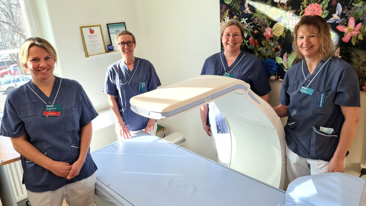 Fyra kvinnor i sjukvårdskläder samlade runt en röntgenapparat, en så kallad DXA.