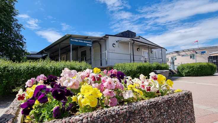 Vit fasad med skylt där det står Norrtälje södra vårdcentral. Blommor i förgrunden.