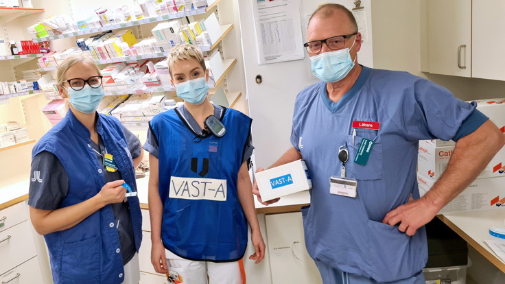 Tre vårdklädda medarbetare med munskydd i läkemedelsförråd