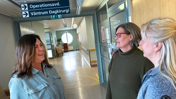 Tre kvinnor står i en korridor. Över dem en skylt med texten "operationsavd"