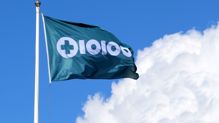 Flagga med Tiohundras logotyp. Blå himmel med sommarmoln.