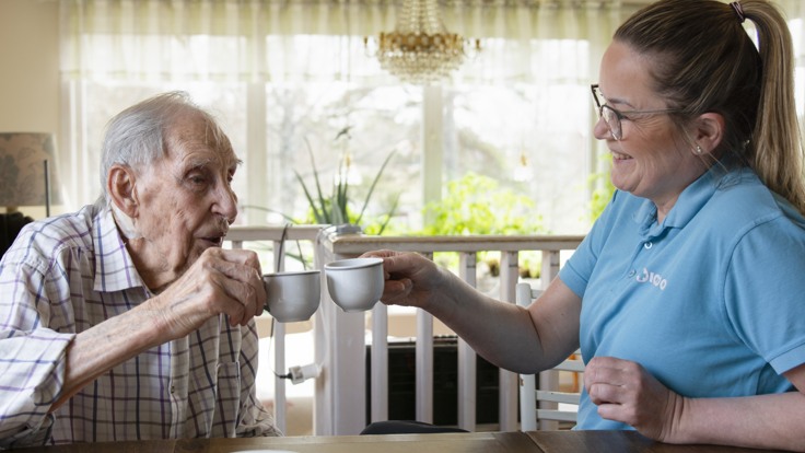 Äldre man och hemtjänstpersonal skålar med kaffekoppar