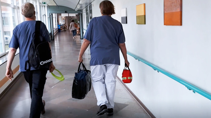 Två sjukvårdsklädda personer med väskor går i korridor.