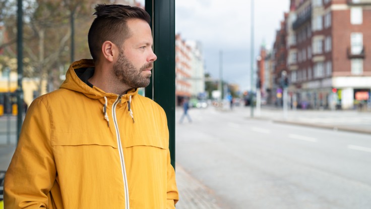 En man står i en busskur på en gata i en stad