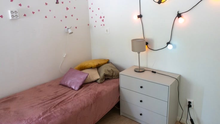Säng med rosa överkast och ljusslinga på väggen