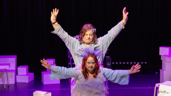 Två kvinnor med utsträckta armar på lila scen